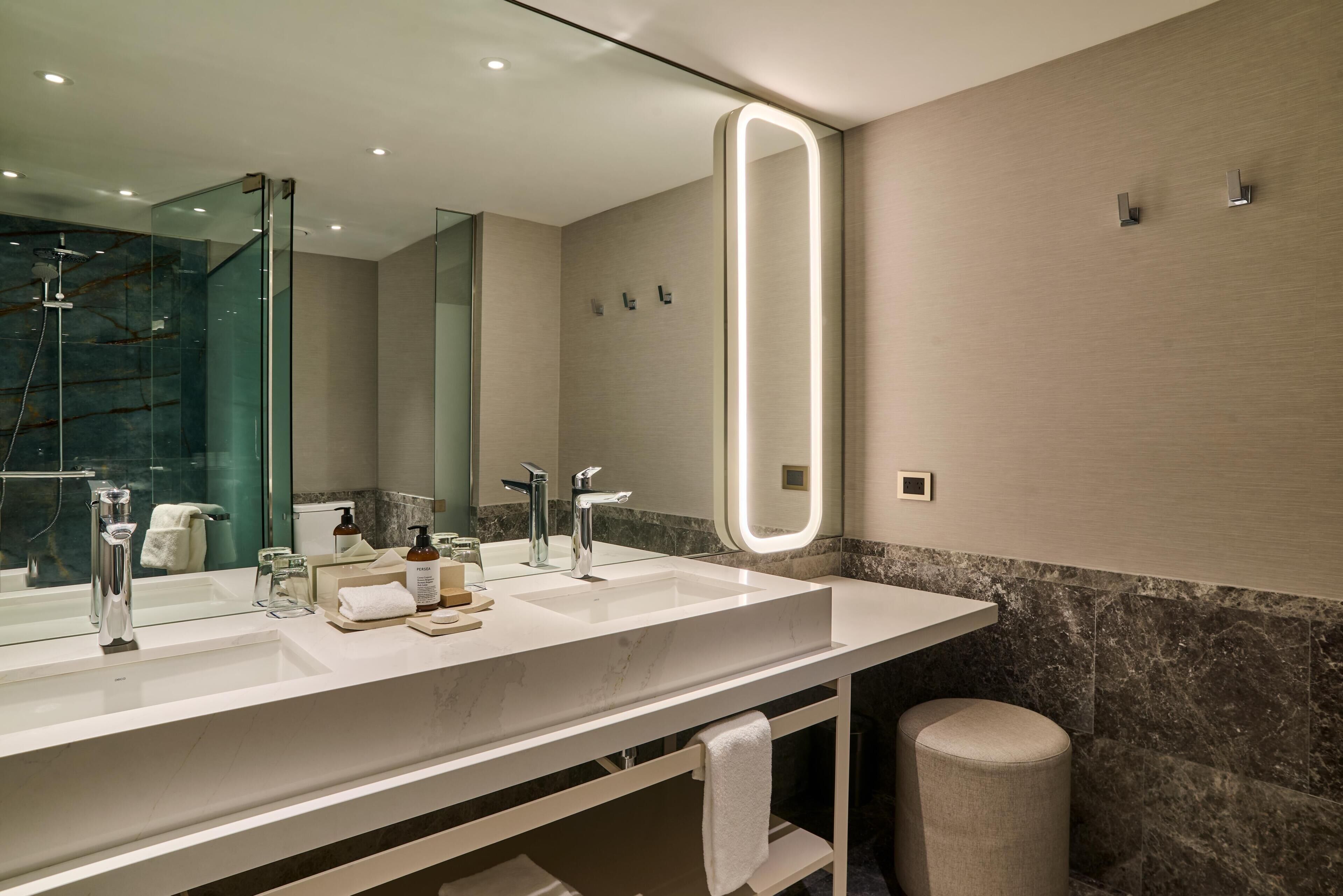 A modern bathroom with a large mirror, two sinks, and a shower.