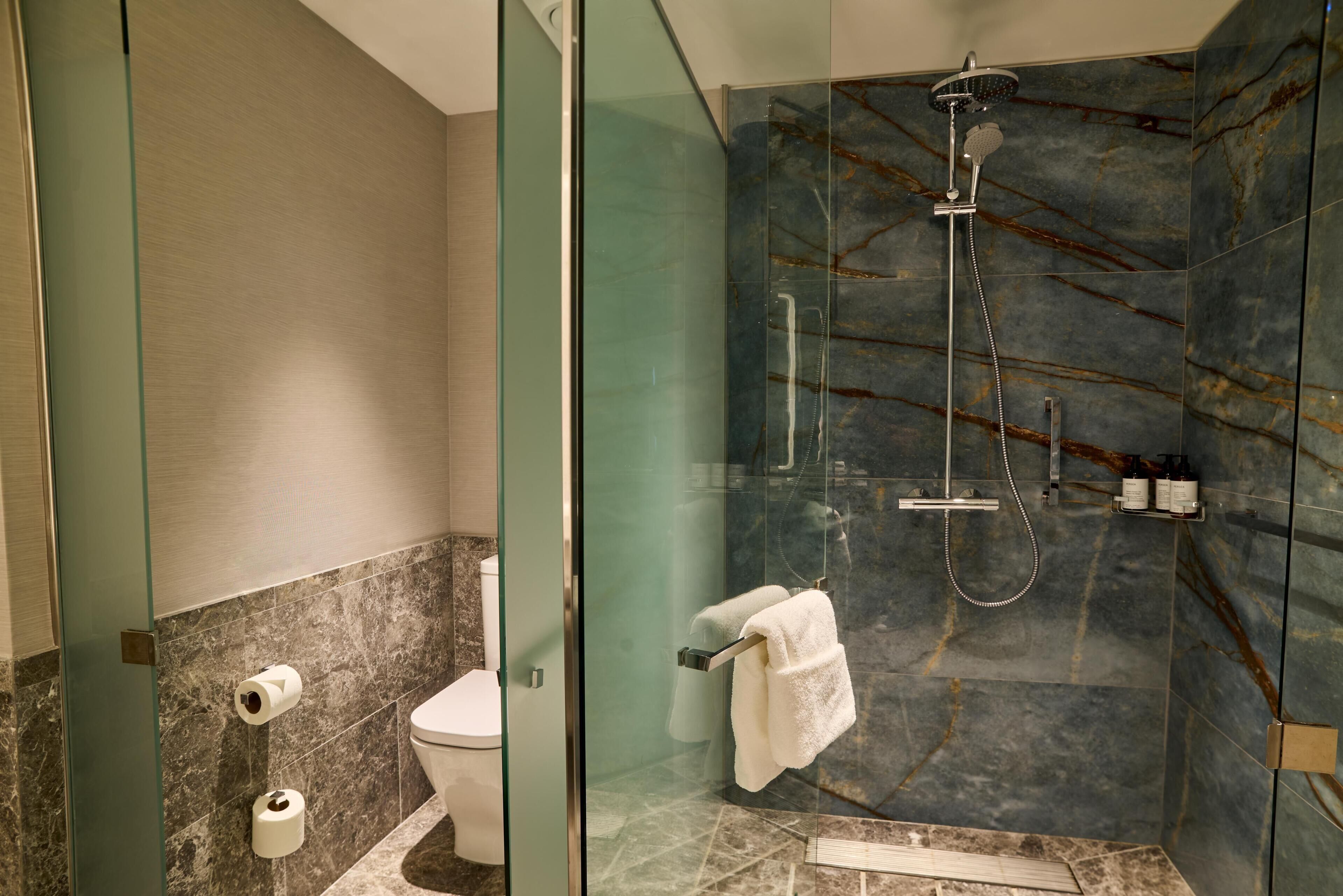 A modern bathroom with a glass-enclosed shower, marble walls, a toilet, and a towel rack.