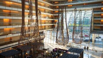 Un hall d’hôtel moderne, avec de nombreux étages, de grandes fenêtres et des éléments décoratifs suspendus.