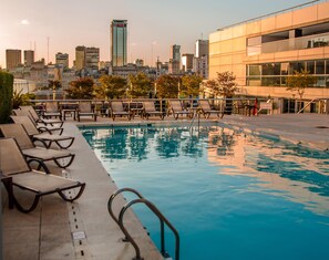 Une piscine sur le toit, avec des chaises longues et une vue panoramique sur la ville en arrière-plan.