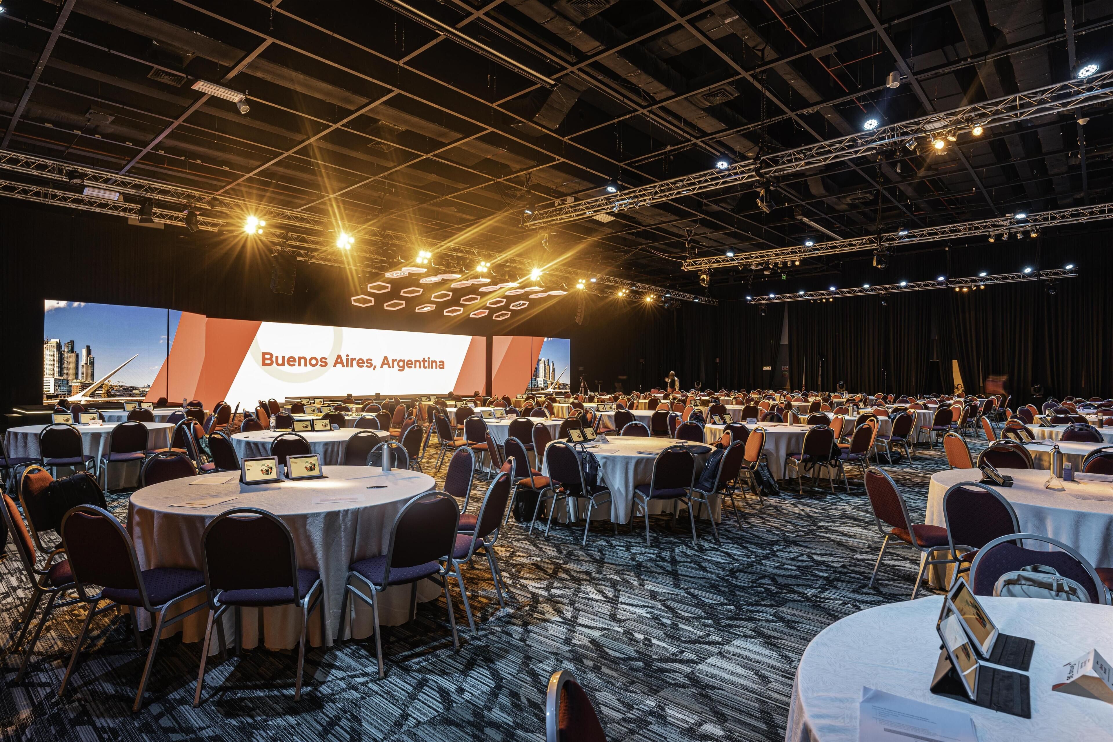 A conference room with round tables, chairs, and a large screen displaying 'Buenos Aires, Argentina'.