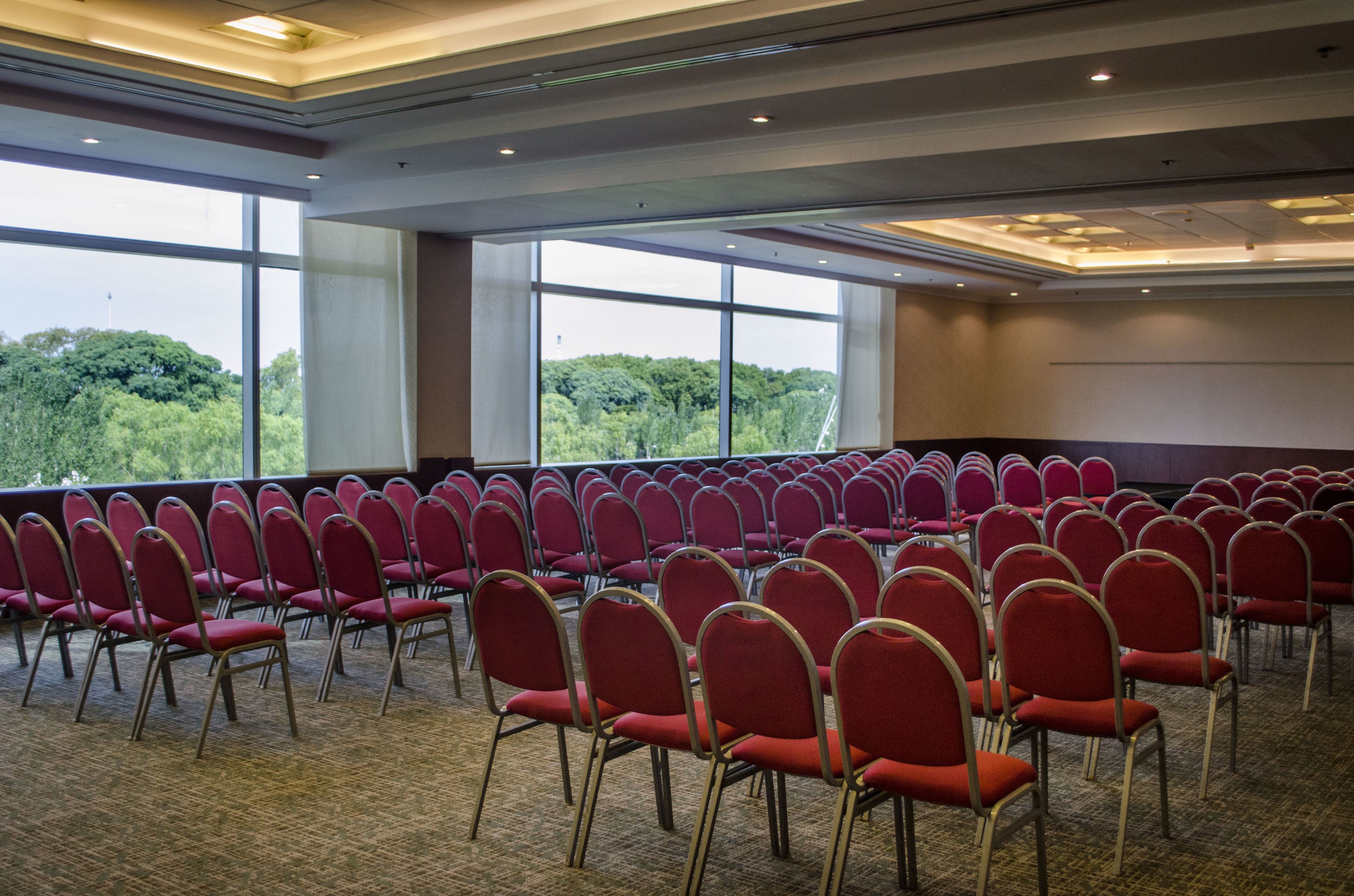 A conference room with rows of red chairs, large windows, and a carpeted floor.