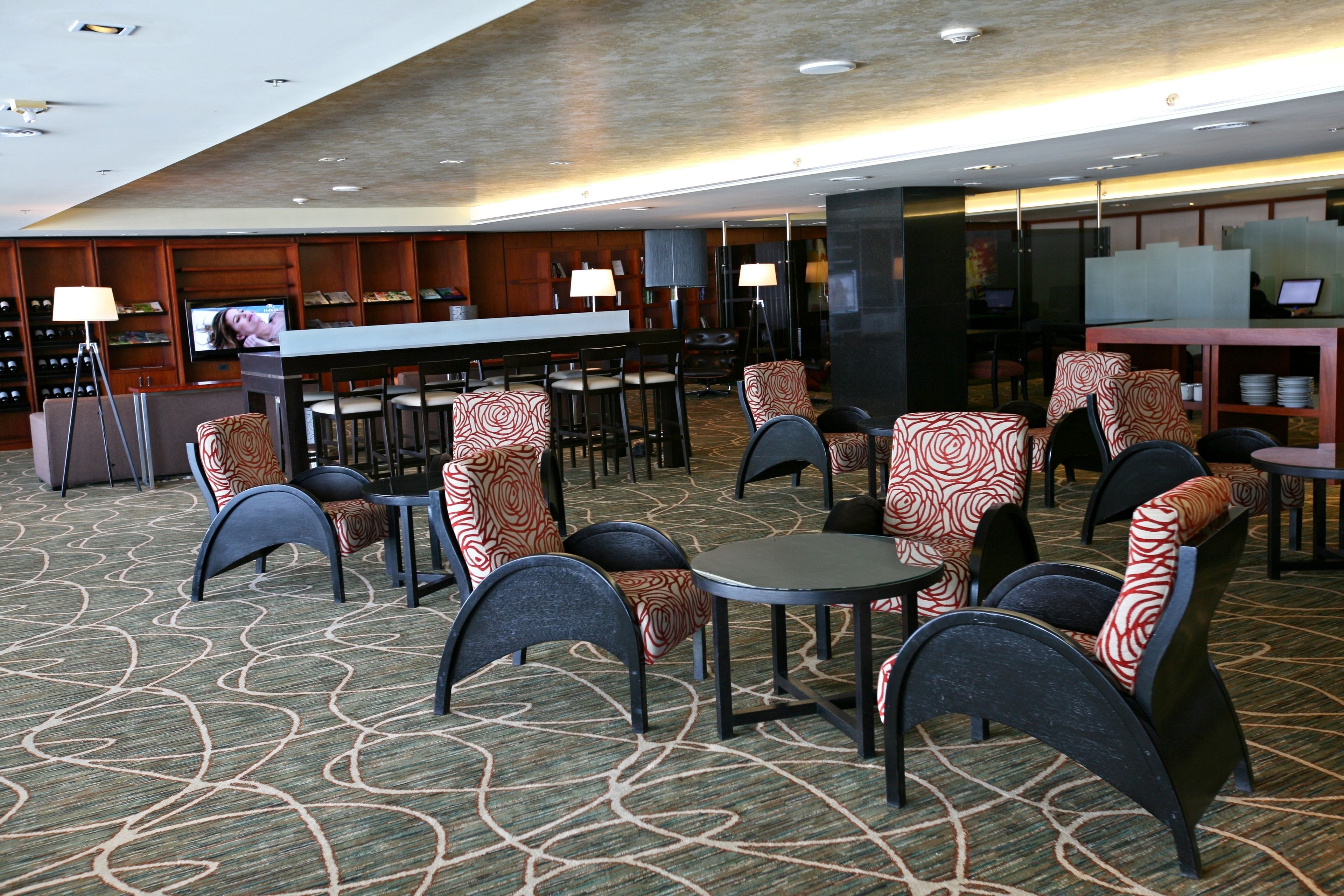 Um hall de hotel com área de bar, espaços para sentar e uma tela de televisão.