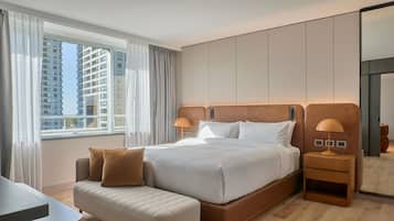 A modern hotel room with a large bed, a bedside table, a small sofa, and a view of tall buildings through the window.