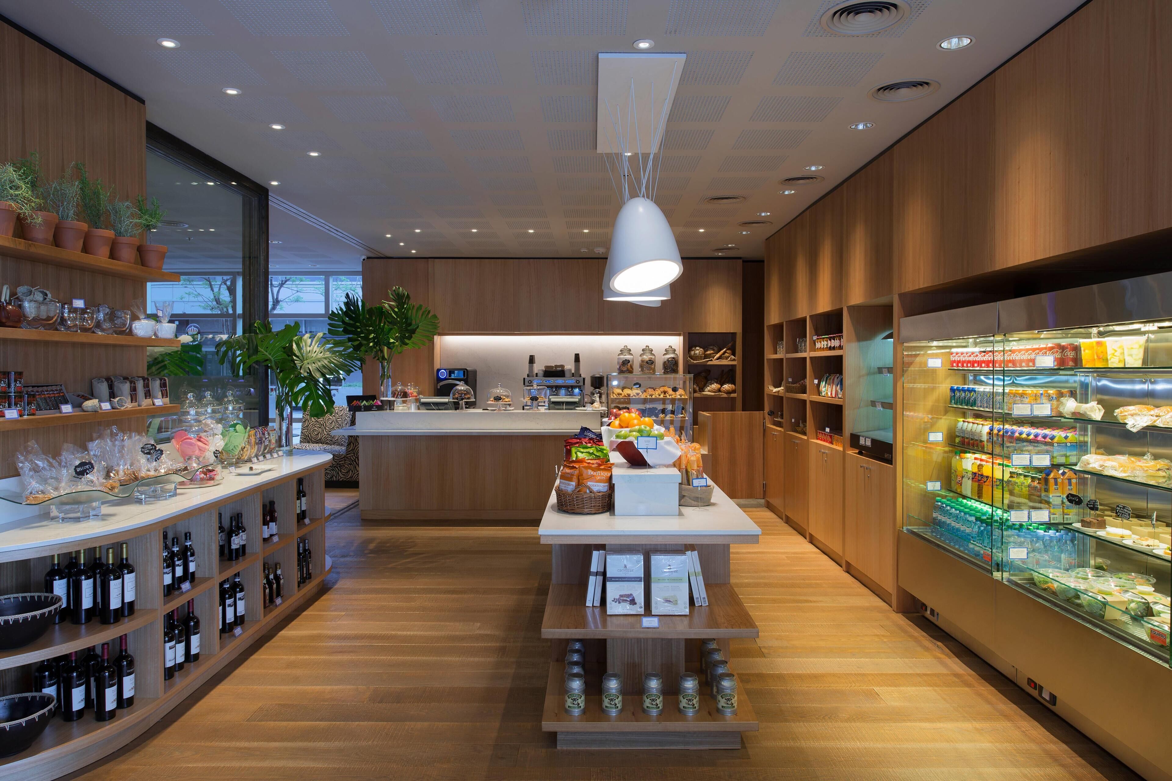 A modern hotel lobby with wooden flooring, a central island with food and beverages, and a glass display case with snacks.