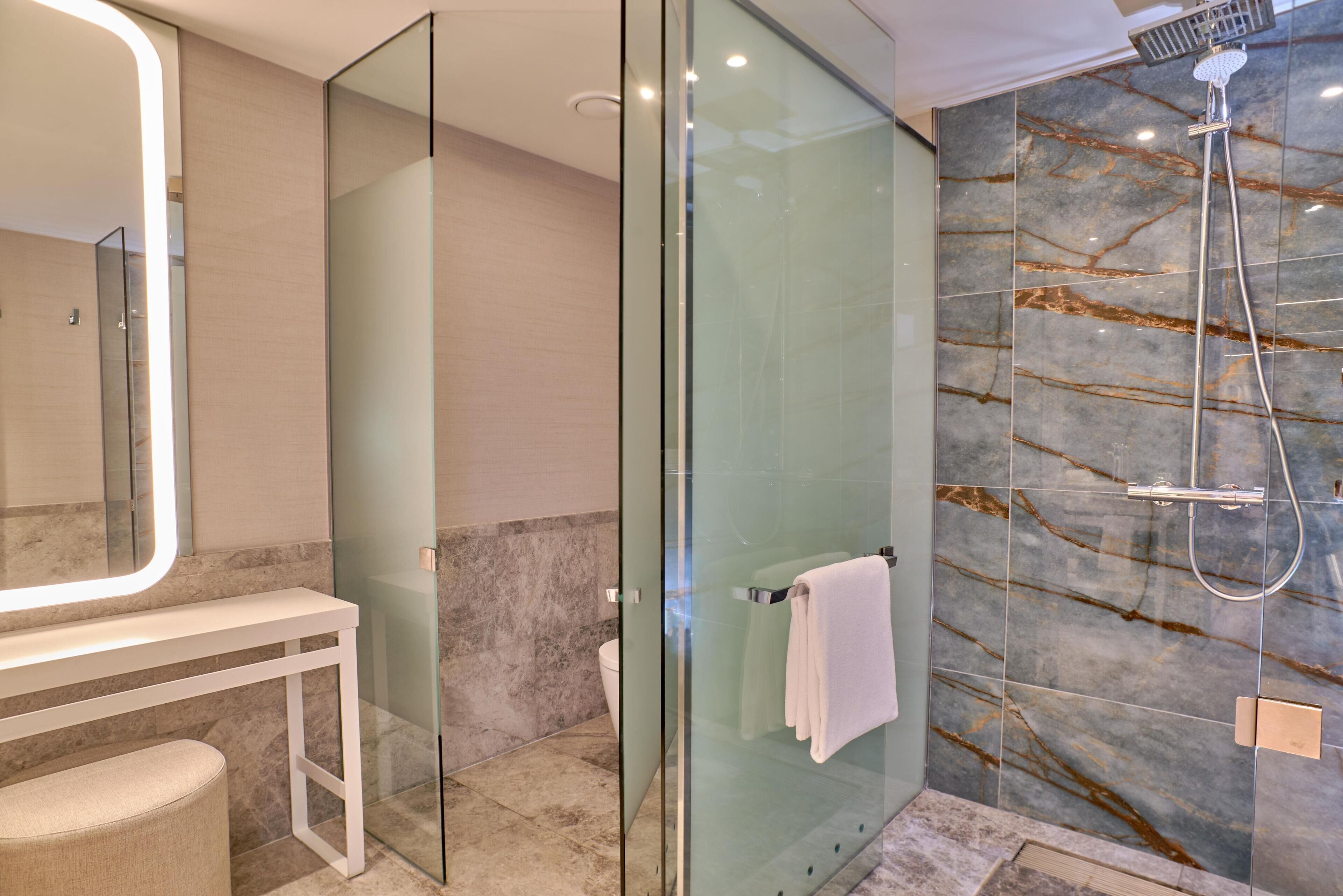 Un baño moderno con cabina de ducha de vidrio, tocador blanco y paredes de mármol.