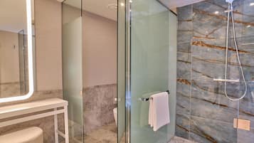 Un baño moderno con cabina de ducha de vidrio, tocador blanco y paredes de mármol.