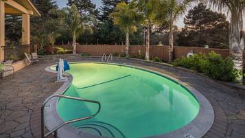 A swimming pool with a stone deck, surrounded by a wooden fence and palm trees.