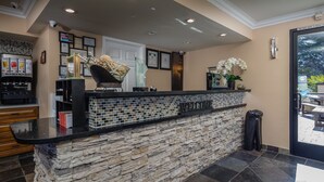A reception area with a stone counter, coffee machine, and framed certificates on the wall. - Stage Coach Lodge (Monterey)