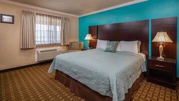 A hotel room with a large bed, two bedside tables with lamps, a window with curtains, and a patterned carpet.