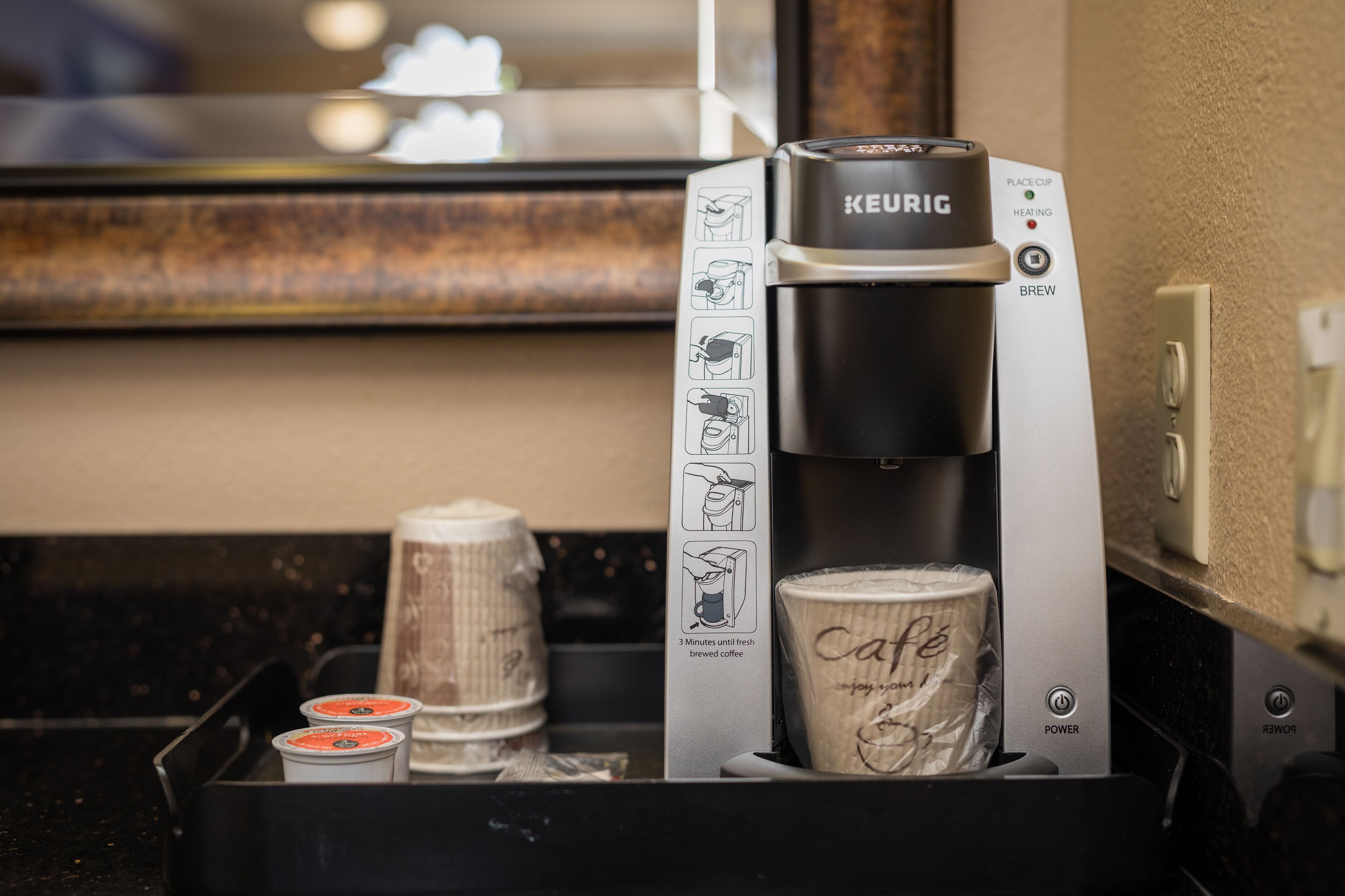 A Keurig coffee machine with a cup of coffee and two coffee pods in a tray.