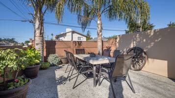 An outdoor patio with a table and chairs, surrounded by potted plants and a palm tree.