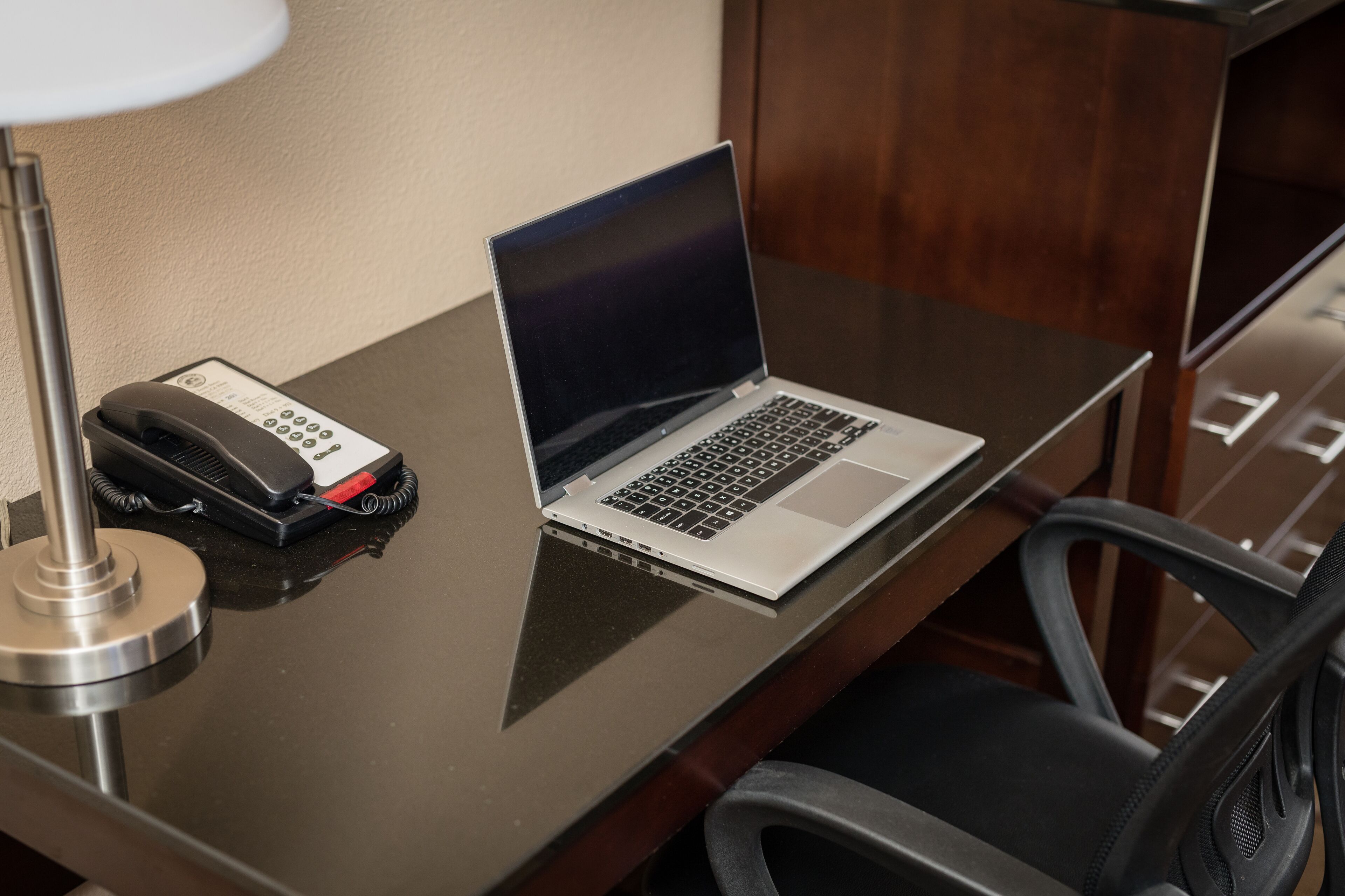 A hotel room desk with a laptop, a telephone, and a lamp.