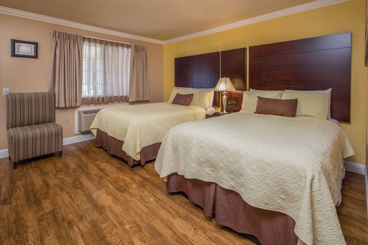 Une chambre d’hôtel avec deux lits, une chaise, une lampe et une fenêtre avec des rideaux.