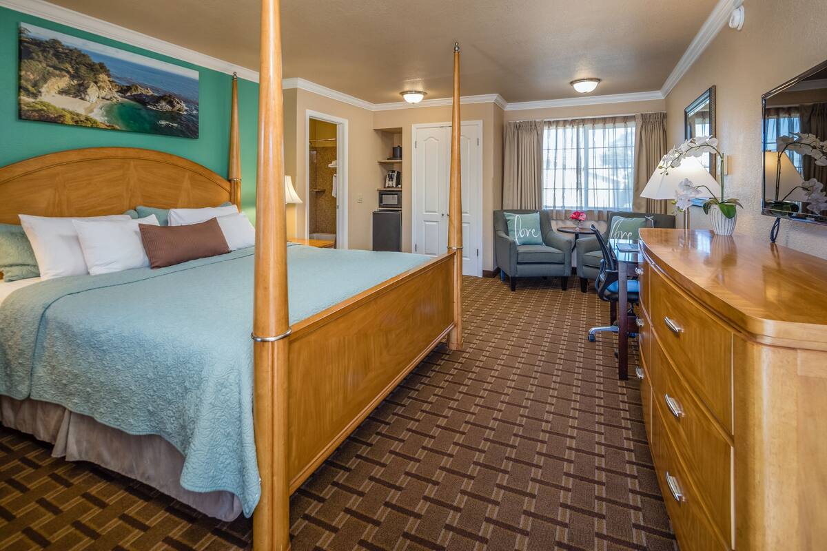 Une chambre d’hôtel avec un grand lit, un bureau, une chaise et une petite table. La salle de bain est équipée d’une douche et de toilettes.