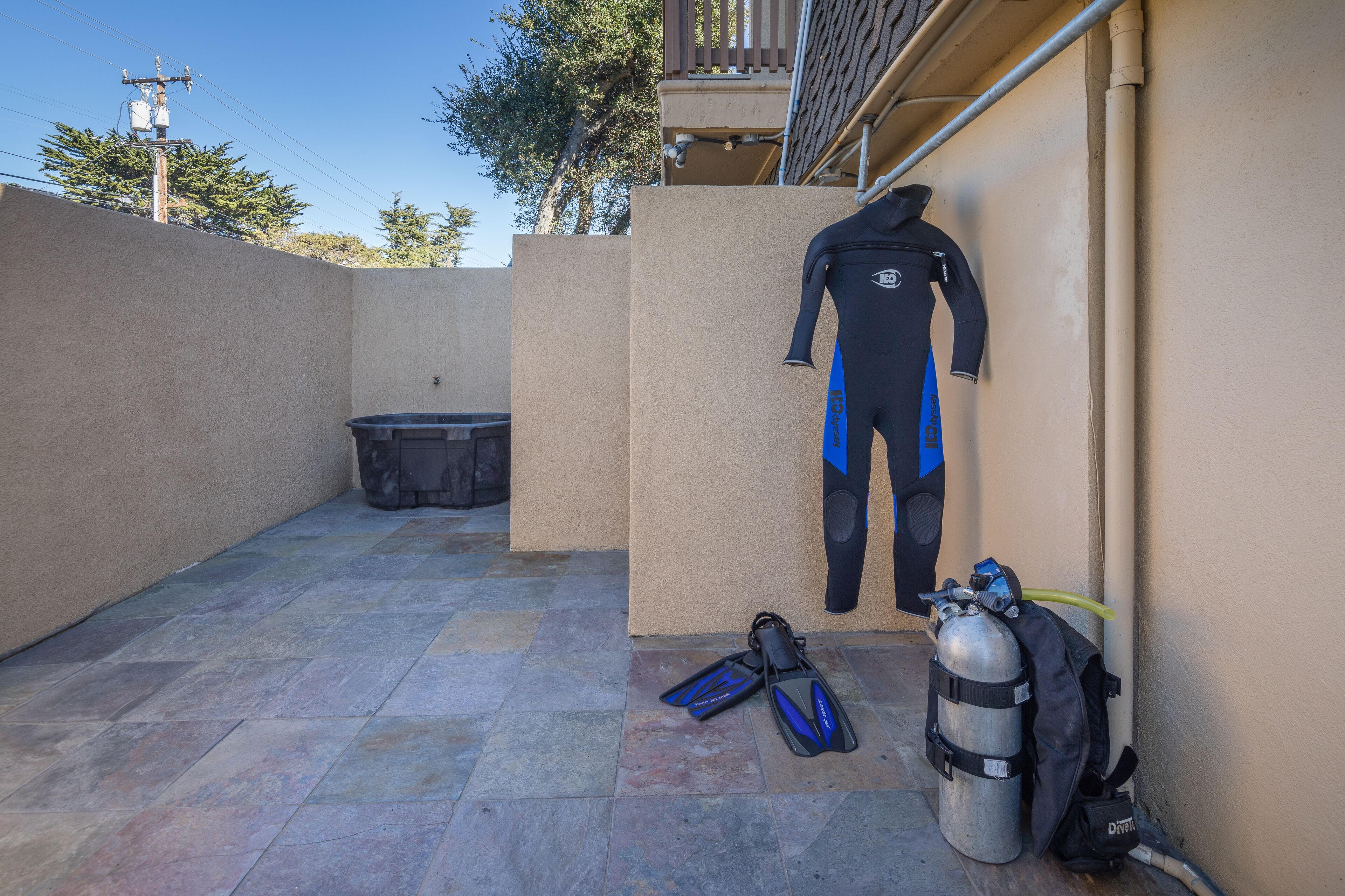 A diving area with a wetsuit, fins, and a scuba tank against a wall.