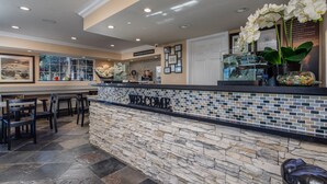 A reception area with a stone counter, framed pictures, and a 'WELCOME' sign. - Stage Coach Lodge (Monterey)