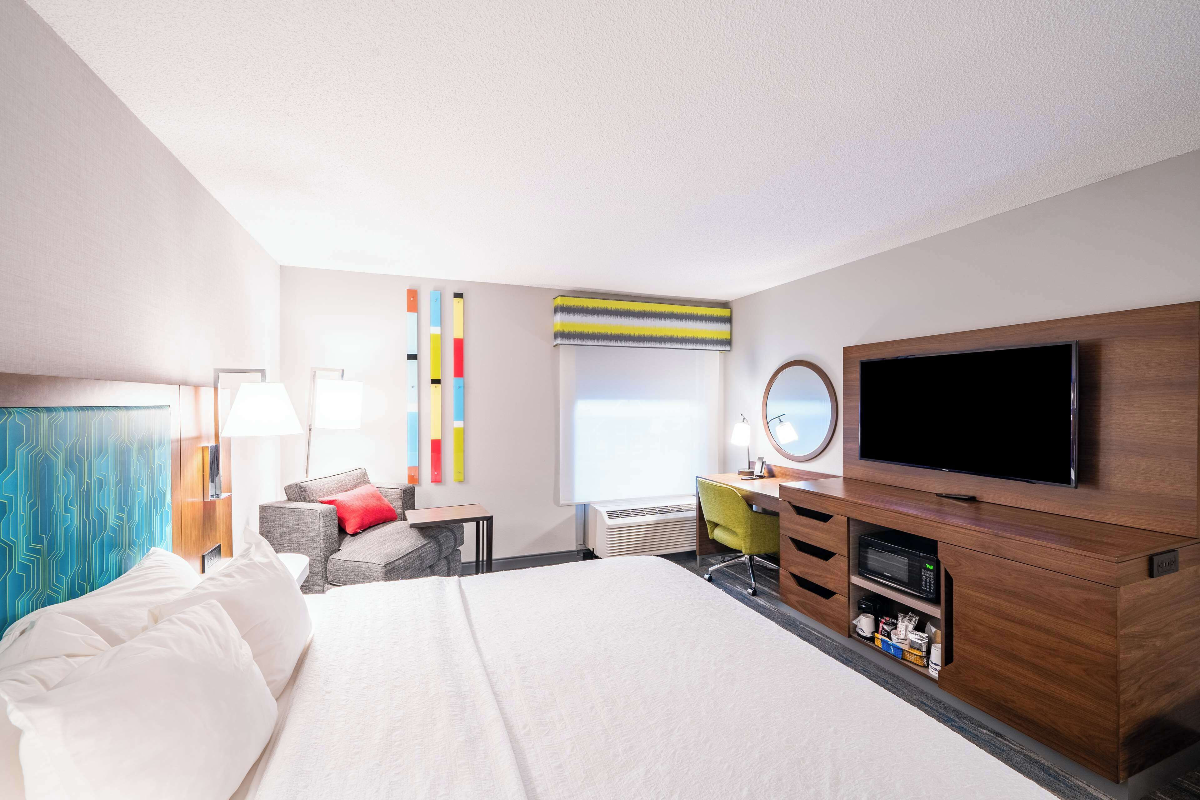 A hotel room with a large bed, a desk with a computer, a flat-screen TV, and a window with a view.