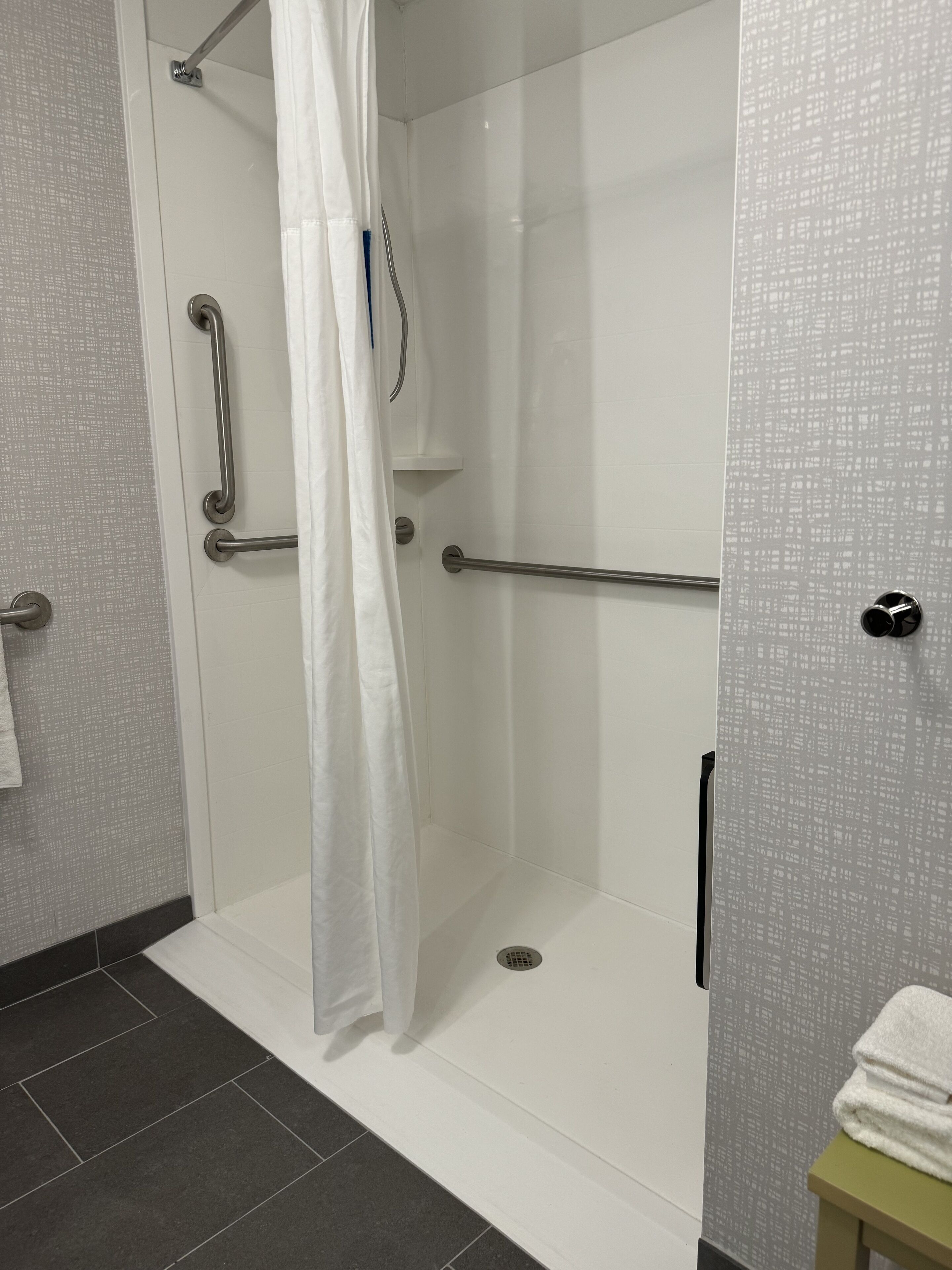 A shower with a glass door, a white towel on a small table, and a handrail.