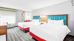A hotel room with two beds, a desk, a chair, a window with blinds, and a wall-mounted air conditioner. - Hampton Inn Lincoln - South/Heritage Park (Lincoln)