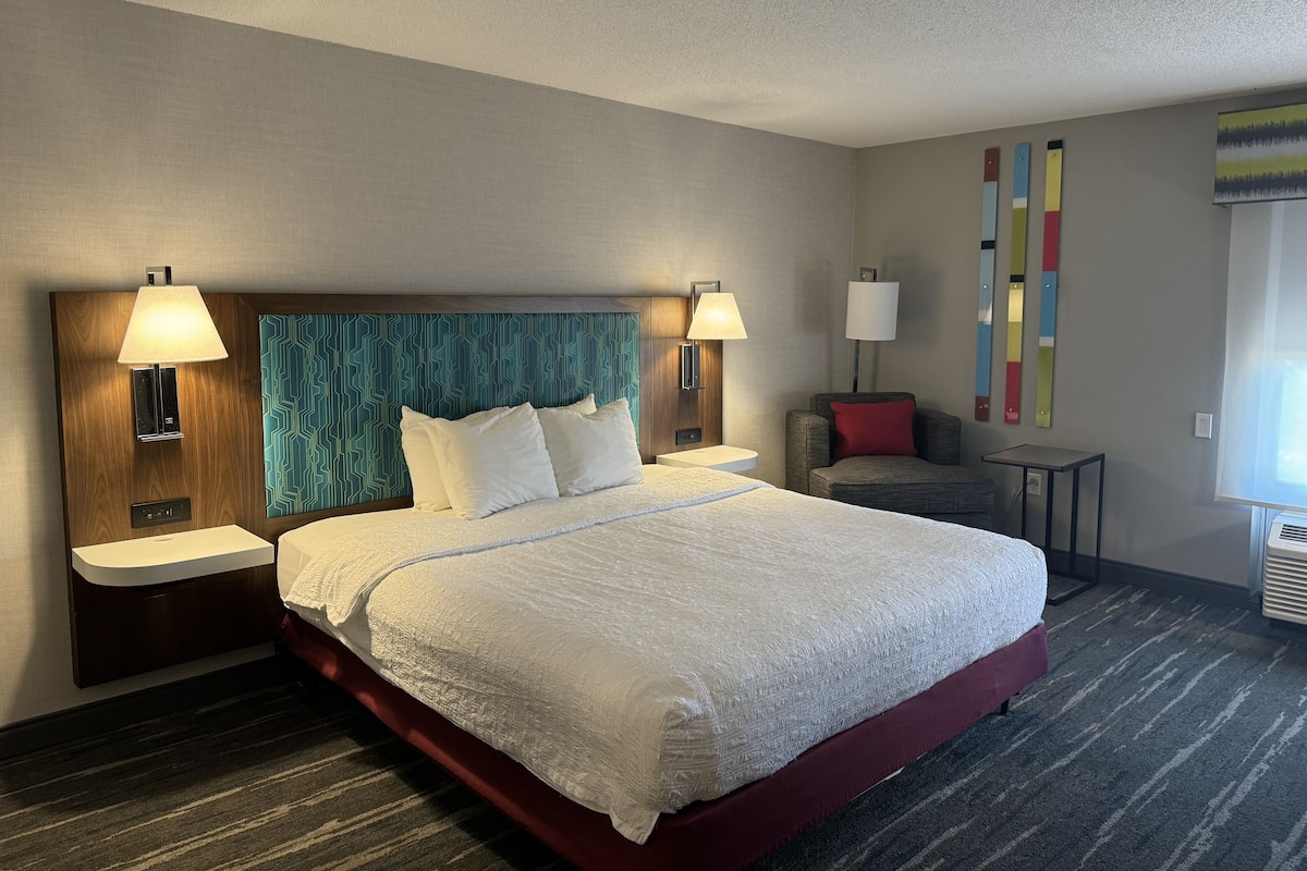A hotel room with a large bed, two bedside tables, a chair, and a small table.