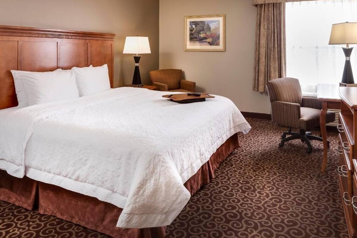A hotel room with a large bed, a desk, two chairs, a lamp, and a framed picture on the wall.