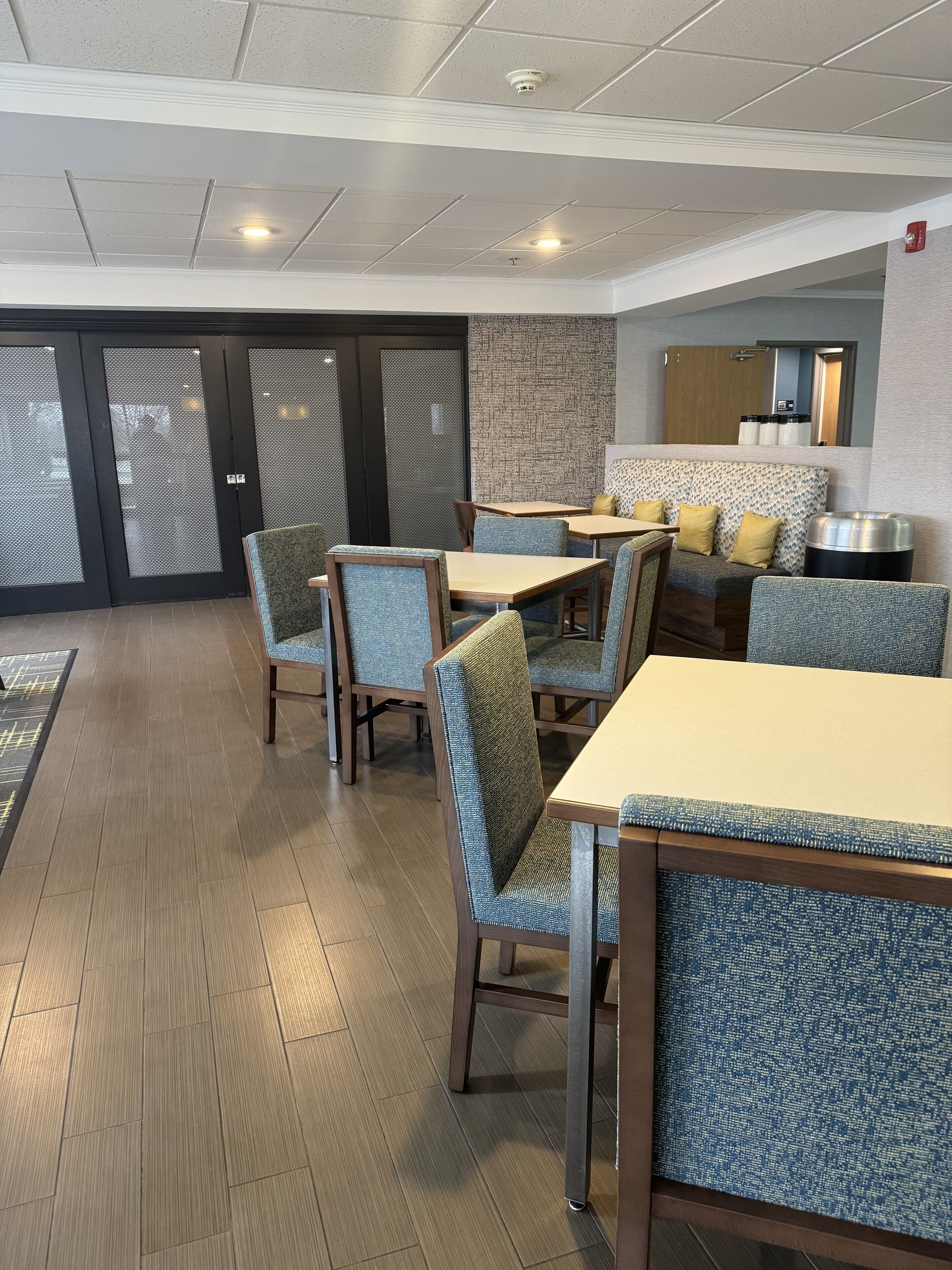 A dining area with tables and chairs, a patterned wall, and a kitchen area with cabinets.