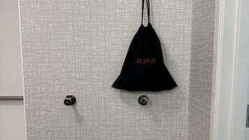 A bathroom with a towel rack holding three towels, a black bag with red text, and a textured wall.