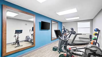 A gym with exercise equipment, a large mirror, and a clock on the wall.