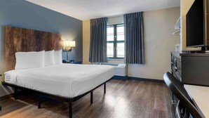 Habitación de hotel con cama, escritorio, televisión y ventana con cortinas.