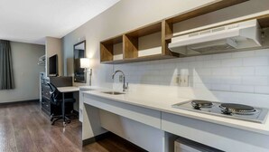 Una cocina moderna con encimera blanca, pileta de acero inoxidable y estufa integrada. Hay un estante de madera sobre la estufa y un espejo en la pared.