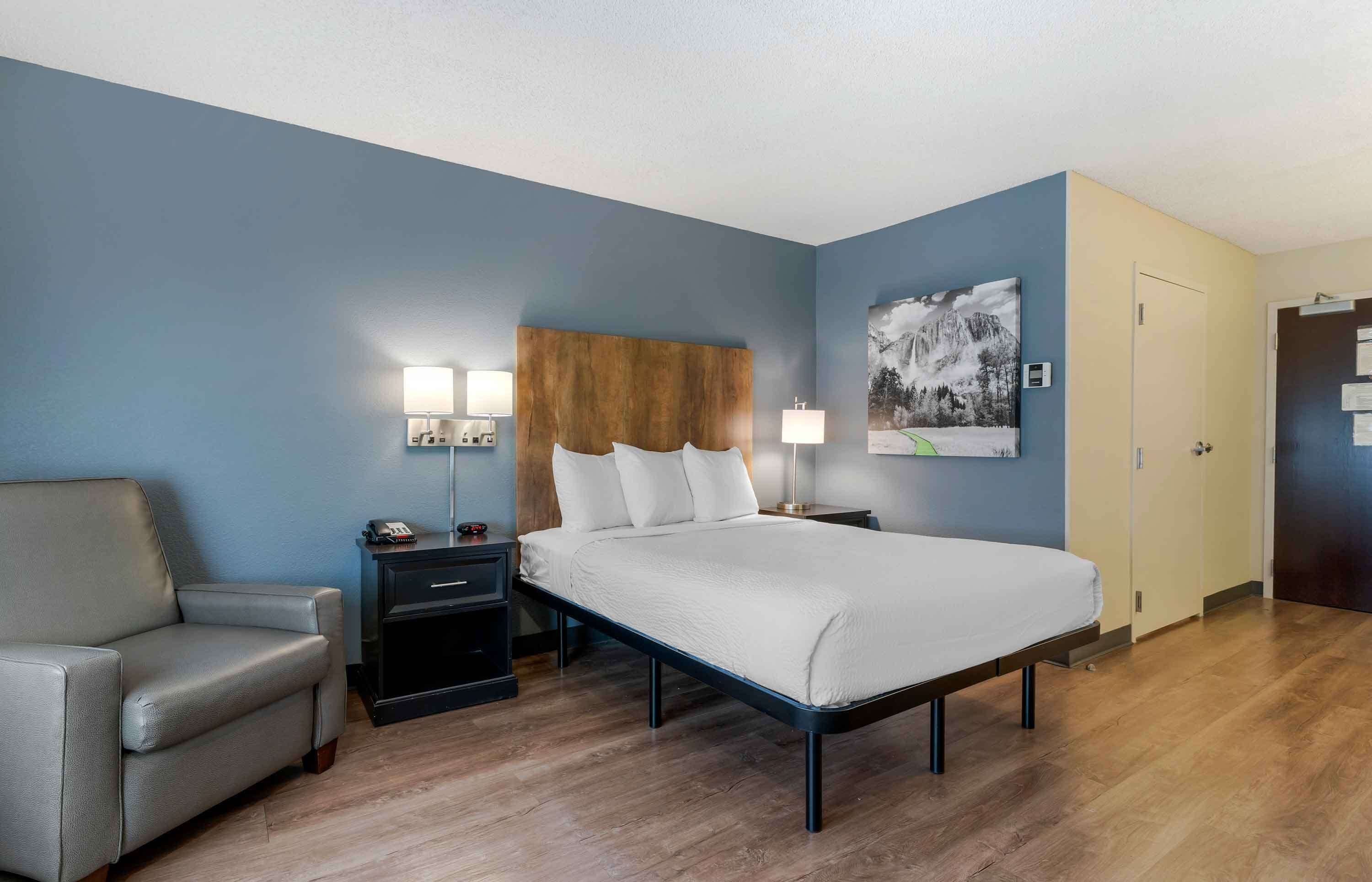 Een hotelkamer met een bed, een stoel, een nachtkastje met lampen en een schilderij aan de muur.