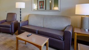 Une chambre d’hôtel avec un canapé en cuir marron, une table basse en bois, une lampe et un miroir au mur.
