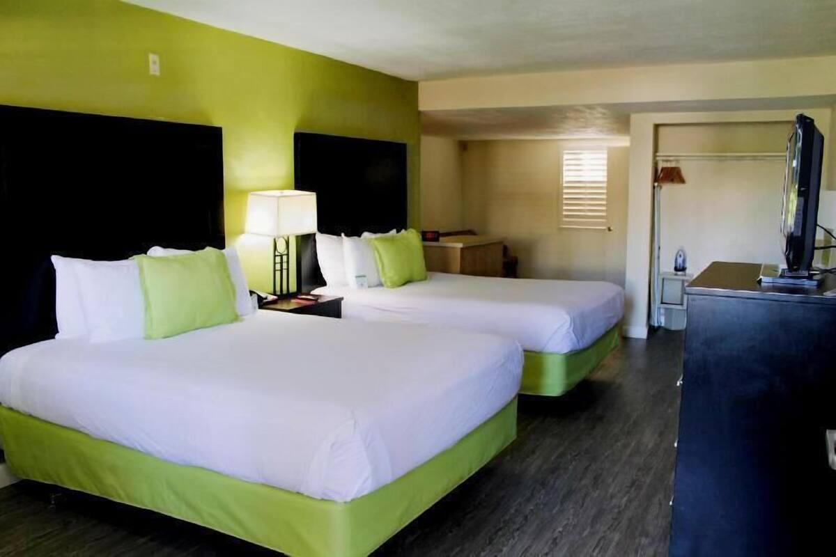 A hotel room with two beds, a desk, a television, and a window with blinds.
