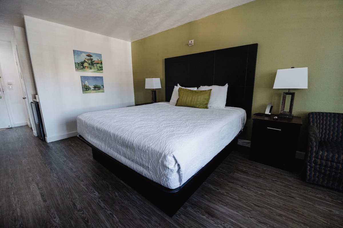A hotel room with a large bed, two bedside tables with lamps, a chair, and two wall-mounted pictures.