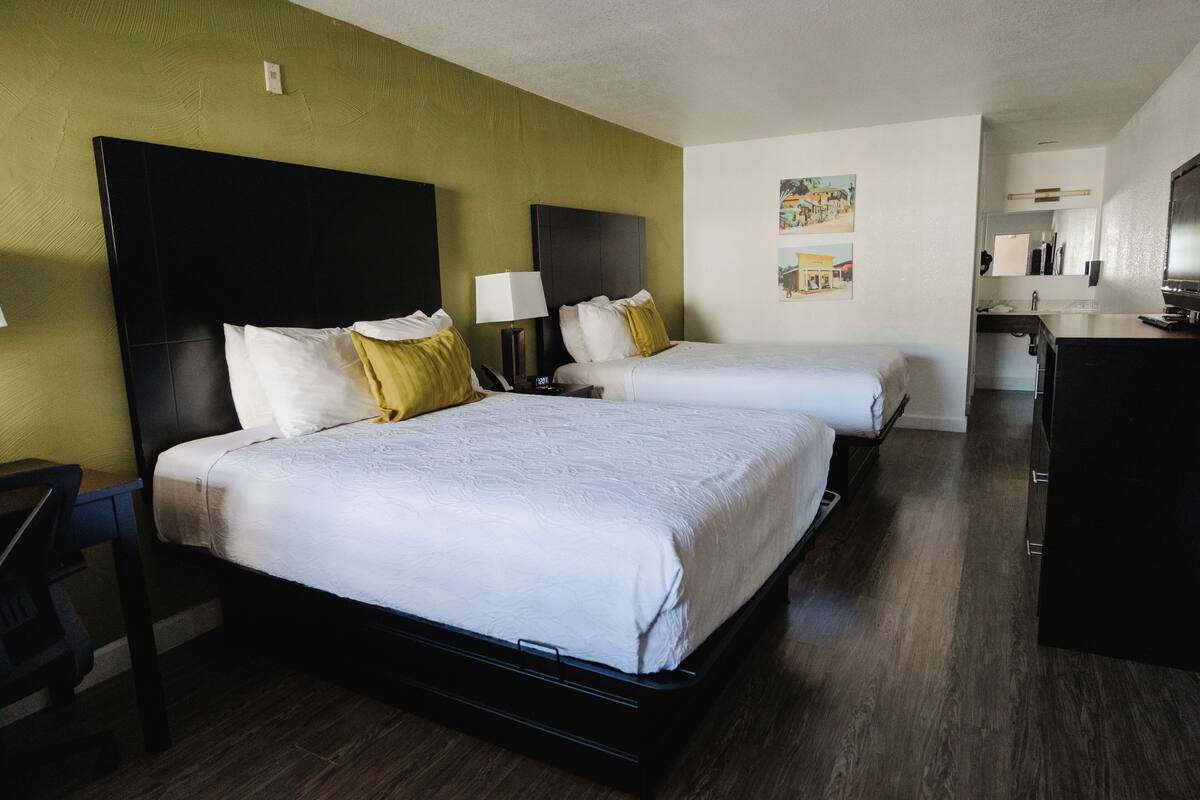 A hotel room with two beds, a desk, and a kitchenette.
