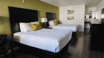 A hotel room with two beds, a desk, and a kitchenette.