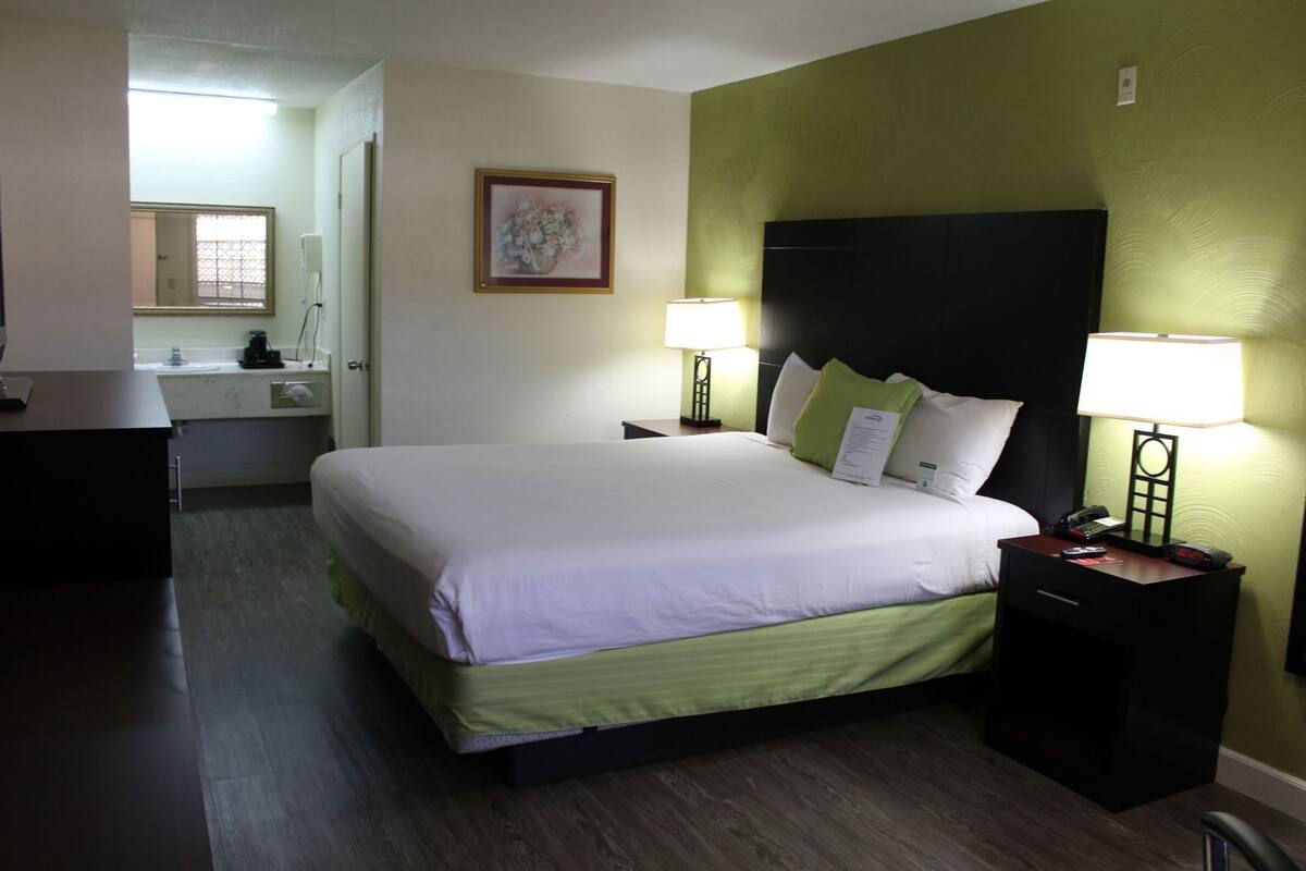 A hotel room with a bed, bedside lamps, a nightstand, a desk, and a mirror.