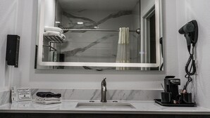 A bathroom with a large mirror, a towel rack, a hairdryer, and a coffee machine. - Old Town Western Inn & Suites (San Diego)
