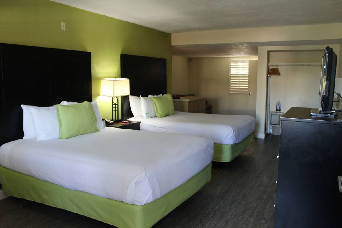 A hotel room with two beds, a desk, a lamp, and a television.