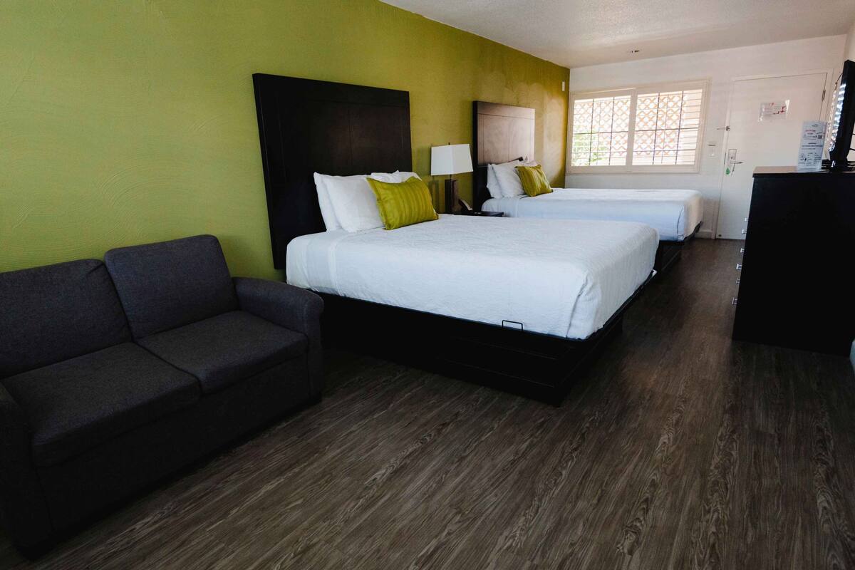 A hotel room with two beds, a sofa, a TV, and a window with blinds.