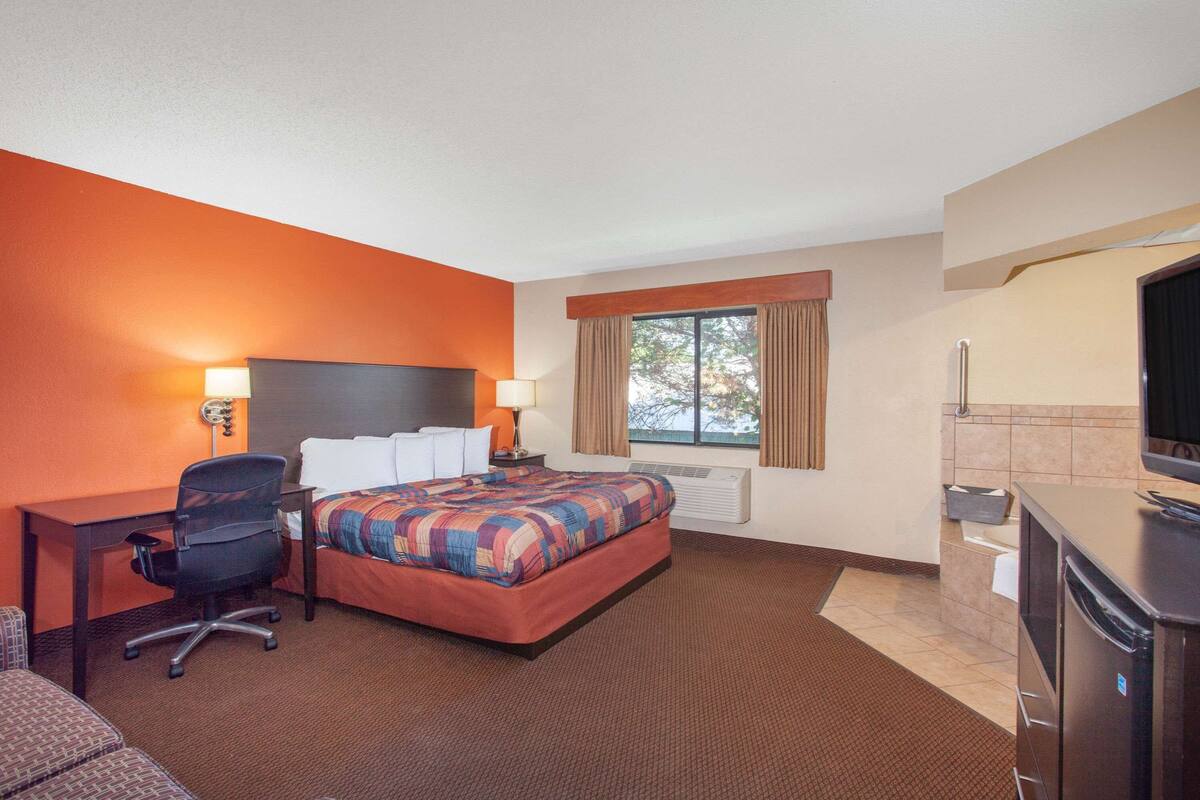 Habitación de hotel con cama, escritorio, silla, televisor y ventana con cortinas.
