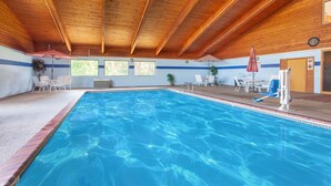 Une piscine intérieure avec des poutres en bois au plafond, un bord de piscine bleu et des chaises longues blanches disposées autour de la piscine.