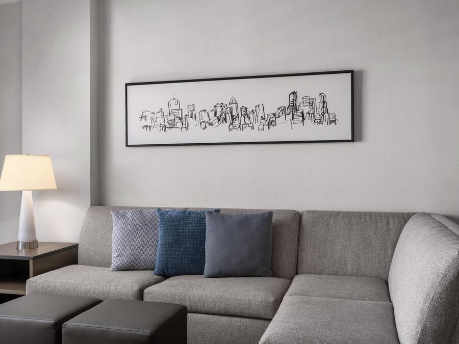 A modern living room with a grey sofa, a side table with a lamp, and a framed cityscape artwork on the wall.
