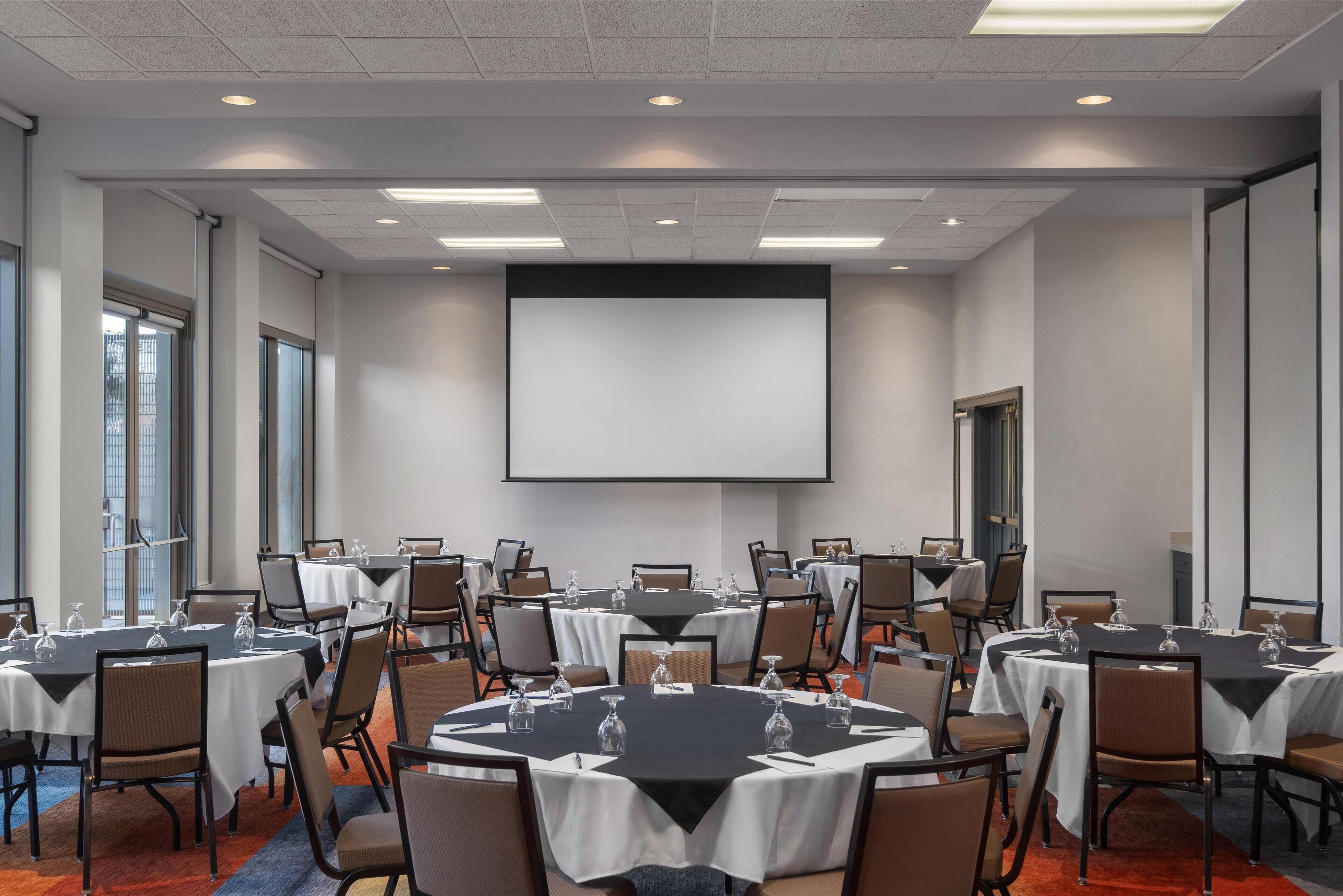 A conference room with multiple tables, chairs, and a large screen.