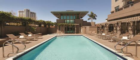 A swimming pool with lounge chairs and a building with a unique architectural design in the background.