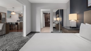 Habitación de hotel con una cama grande, un escritorio, una silla, una lámpara y un espejo.