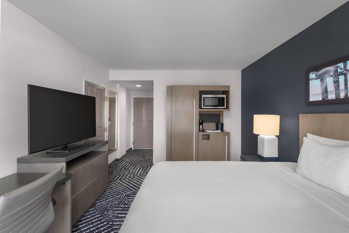A hotel room with a bed, a TV, a microwave, a lamp, and a small kitchenette.