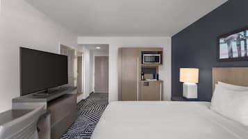 Habitación de hotel con cama, televisión, microondas, lámpara y una pequeña kitchenette.