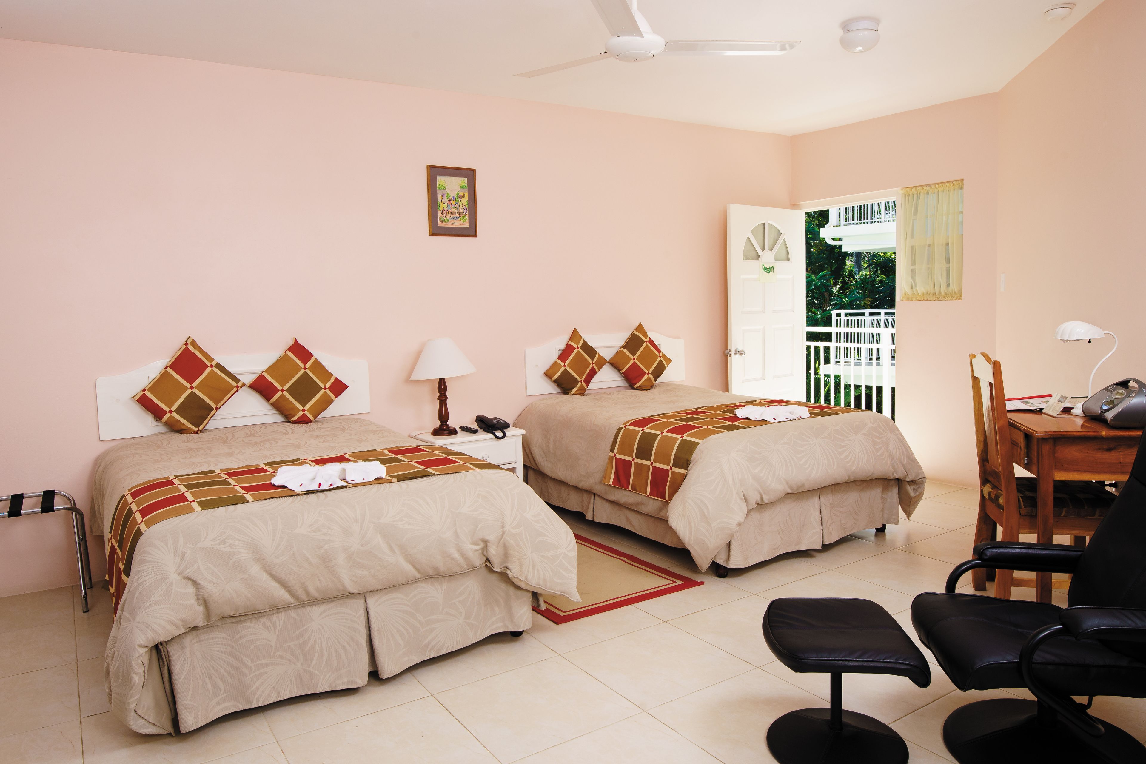 A hotel room with two beds, a desk, a chair, a lamp, and a window with a view of a balcony.